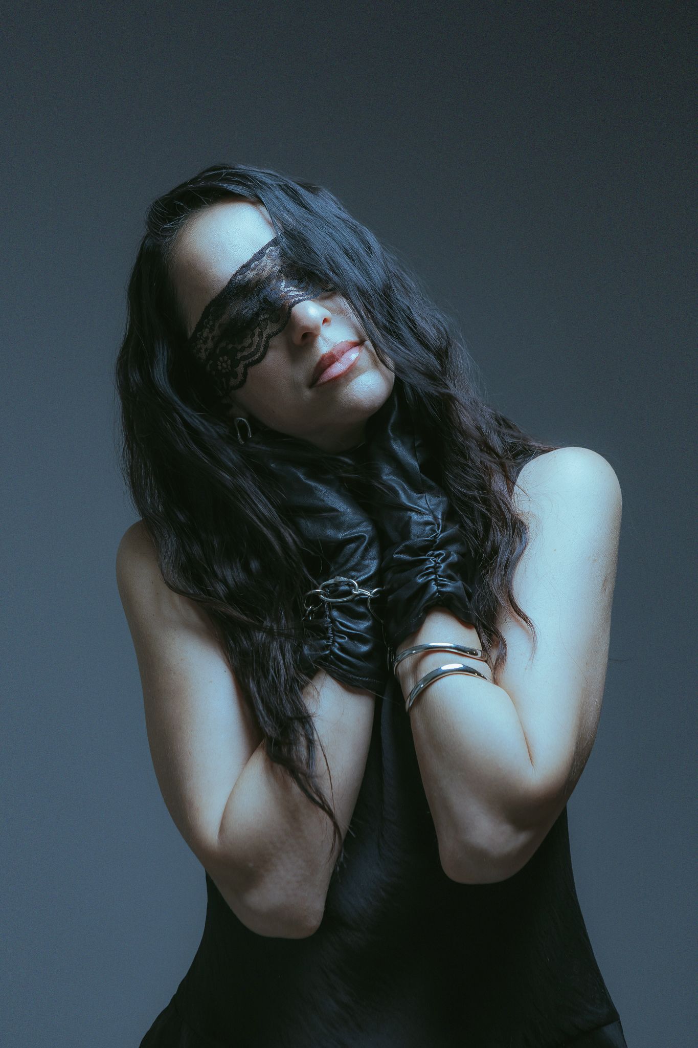 Sole Llorente with black lace over her eyes and leather gloves at her collarbone, against a blue-grey backdrop
