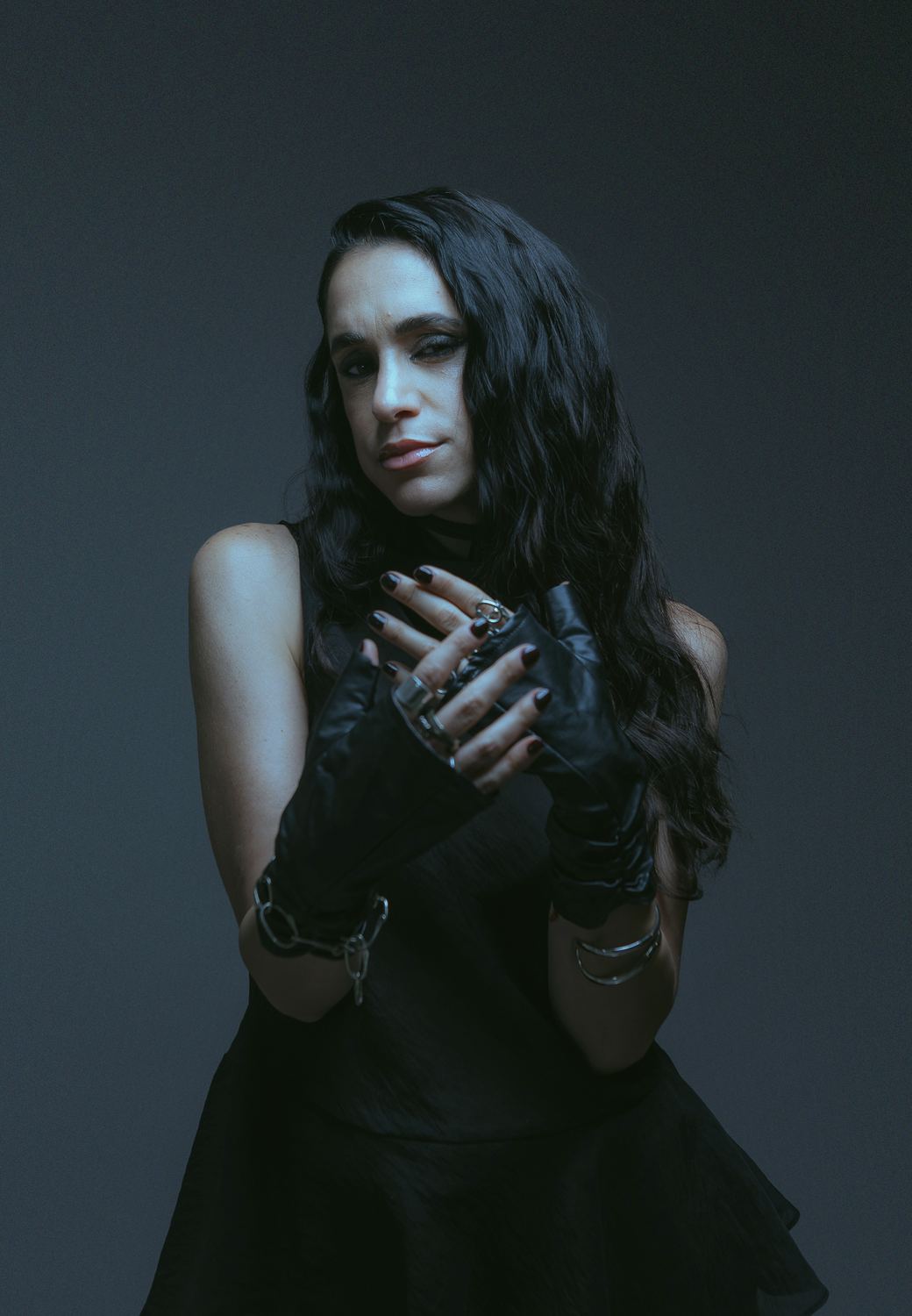 Leather gloves and rings, hands at her collarbone, dark blue backdrop