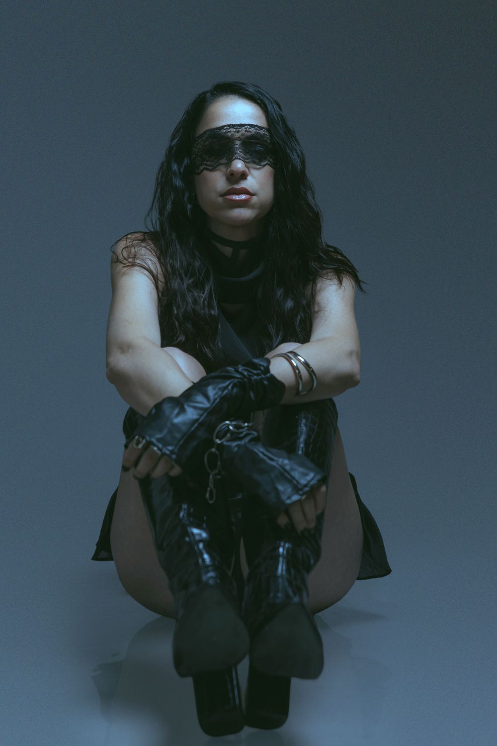 Seated on the floor in a lace mask and gloves