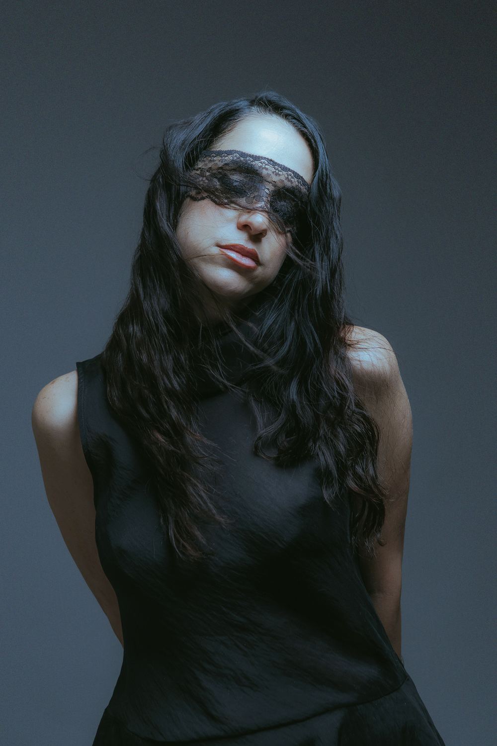 Black lace over her eyes, hands behind her back