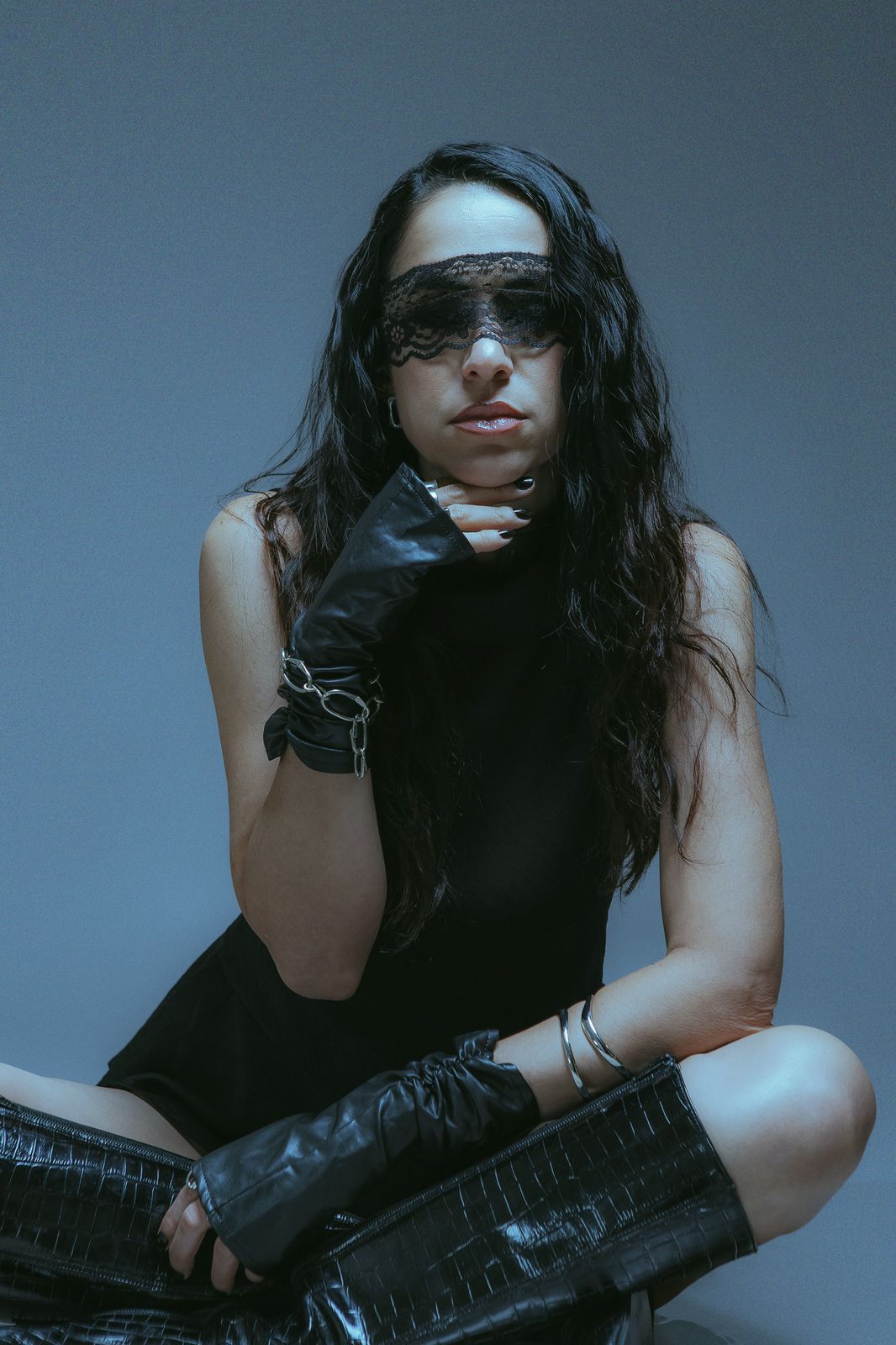 Sole Llorente seated on the floor in a lace mask, a gloved hand at her chin